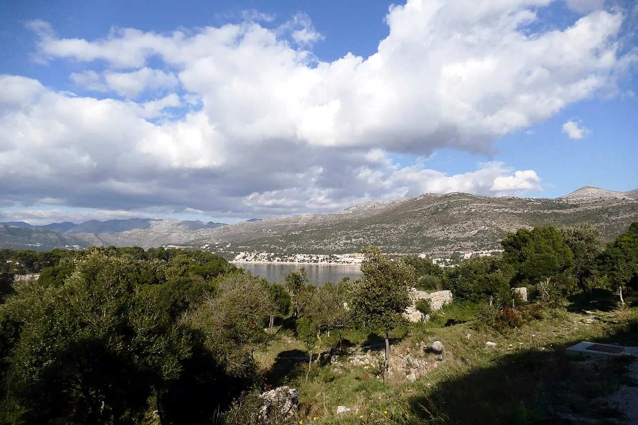 A view over a bay near Dubrovnik towards a coastal town under bare limestone mountains, the Croatian side where the day trip starts