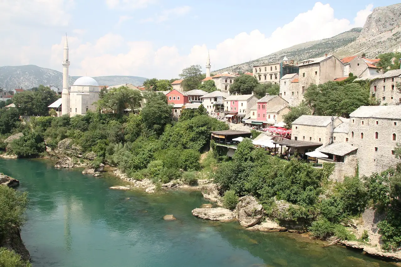 The Neretva running green past the stone houses, mosque dome and minaret of Mostar old town, bare karst hills behind
