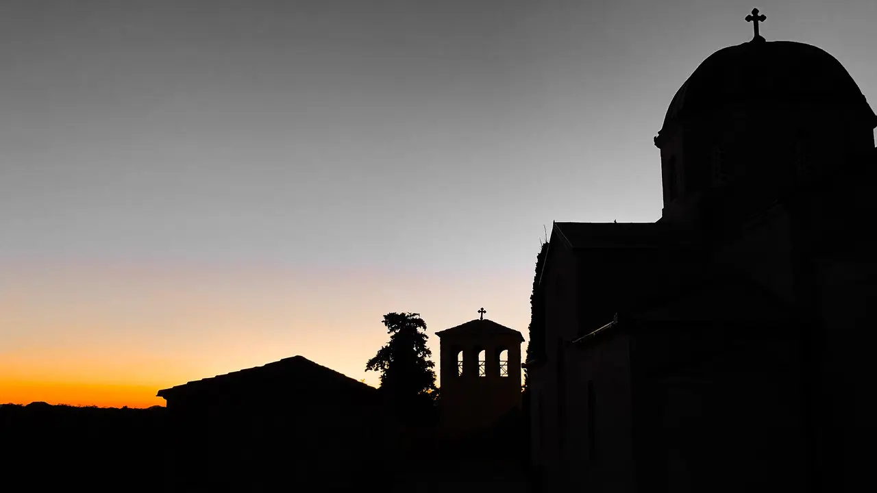 The dome and belfry of Tvrdos monastery near Trebinje in silhouette against an orange sunset sky