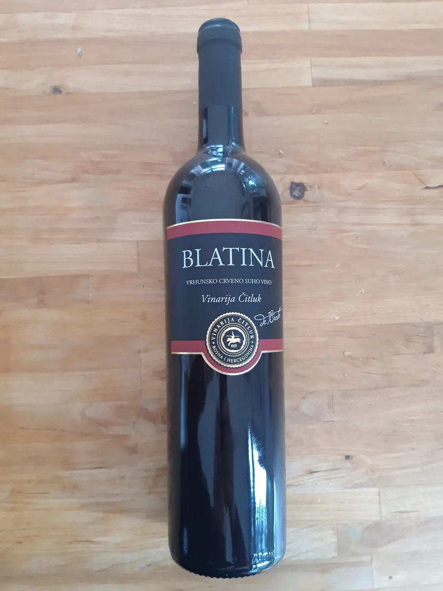 A bottle of Blatina dry red wine from Vinarija Čitluk standing on a wooden table
