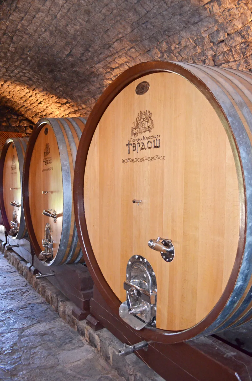 Large oval oak wine casks branded Tvrdoš in the stone vaulted cellar of Tvrdoš Monastery near Trebinje
