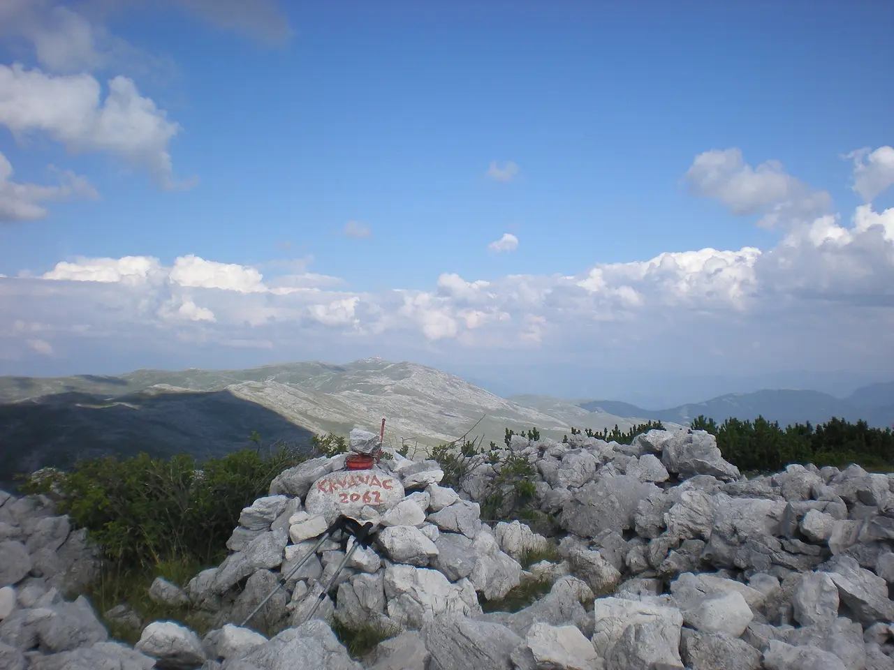 A hand-painted summit stone and trekking poles on a rocky top of the Bjelasnica ridge in summer