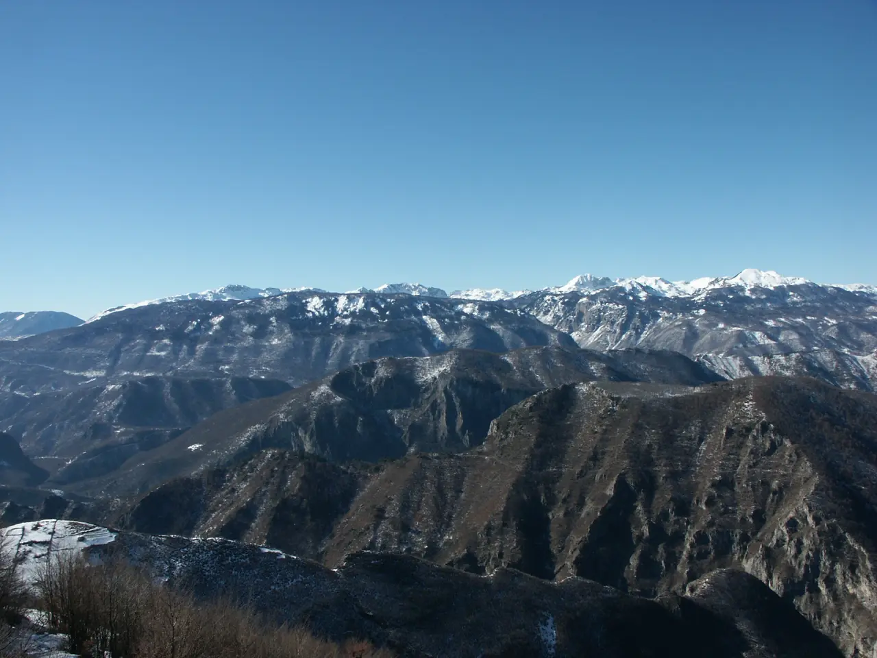 A cold-season view from the Visocica ridge across dark forested valleys to the snow-streaked wall of Prenj