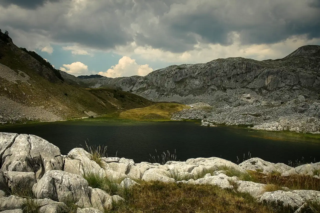 A dark glacial lake on the Zelengora massif framed by white karst slabs under heavy storm cloud