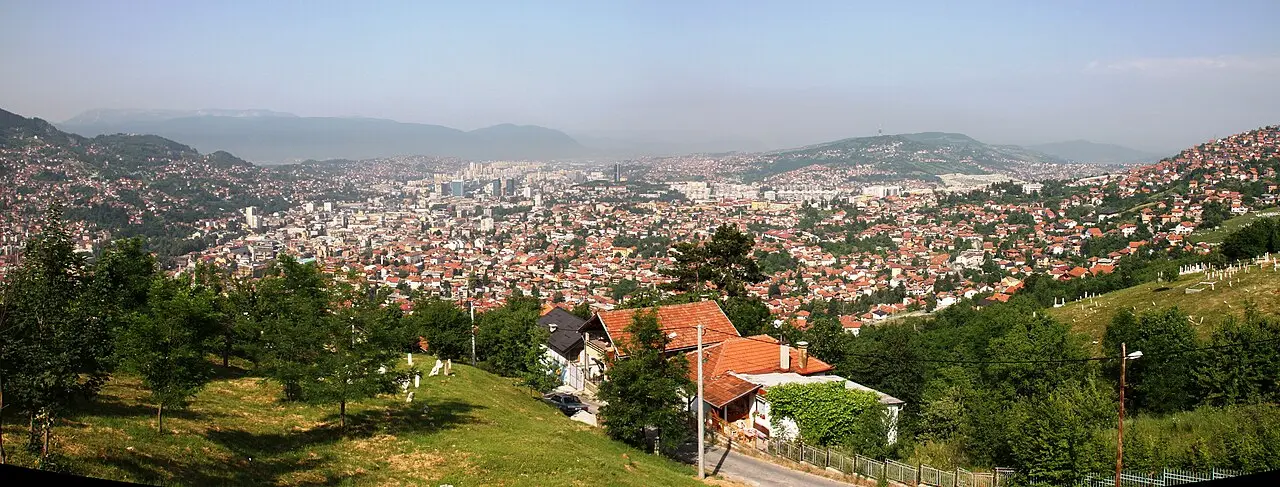 Panorama of Sarajevo filling its valley, minarets and red roofs with wooded hills rising on both sides