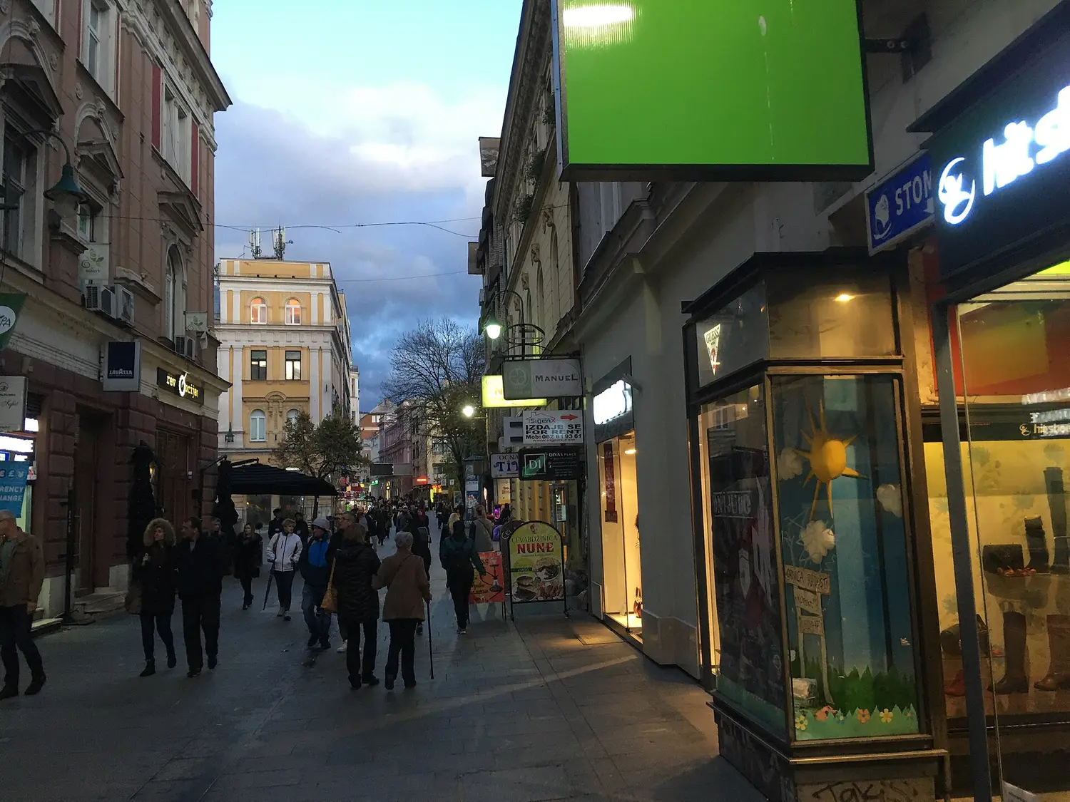 A busy central street in Sarajevo with people walking past shops and cafes on an ordinary day