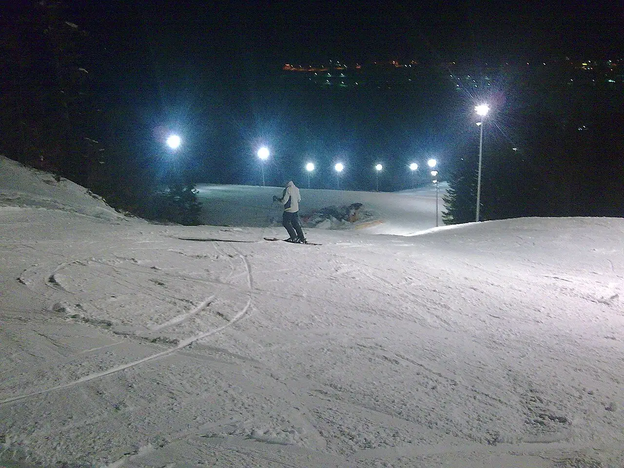 Floodlit night skiing on Bjelašnica with a packed piste and a chairlift under a dark sky