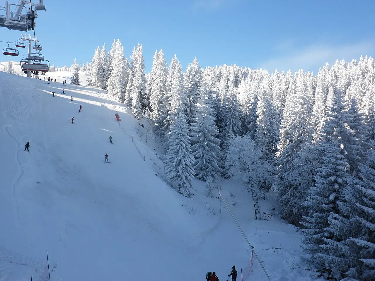 Skiers and a chairlift on the wide Ogorjelica piste at Jahorina on an overcast day