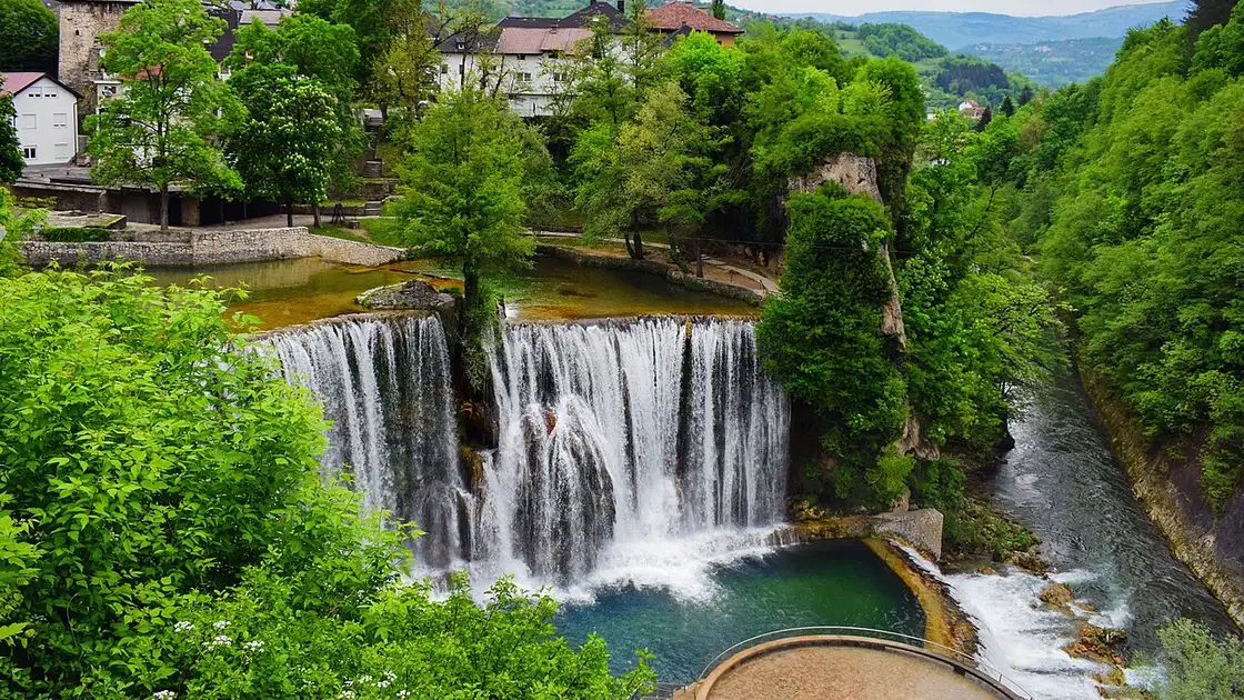 The Pliva Waterfall pouring over a wide tufa ledge in the centre of Jajce, the old town rising on the hill behind it