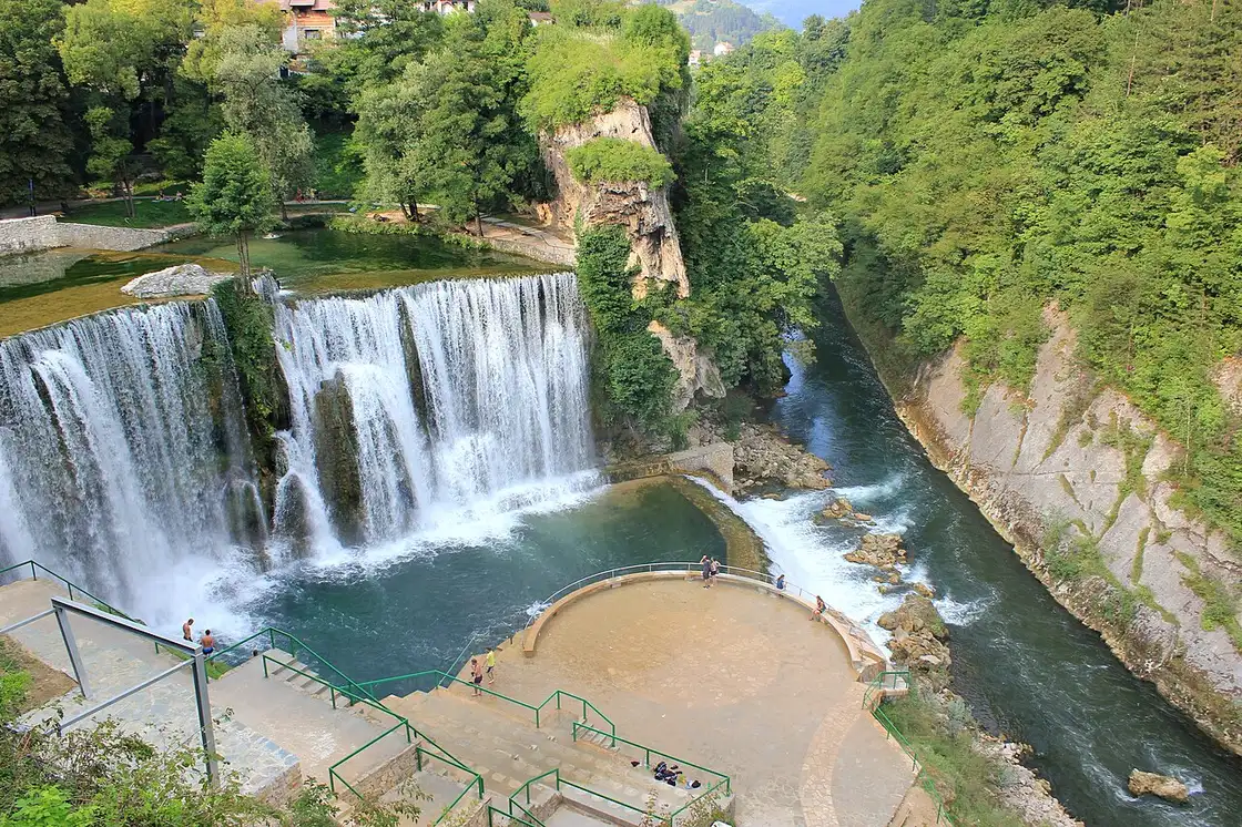 The Pliva Waterfall in Jajce seen close up, a wide curtain of white water over a green tufa ledge