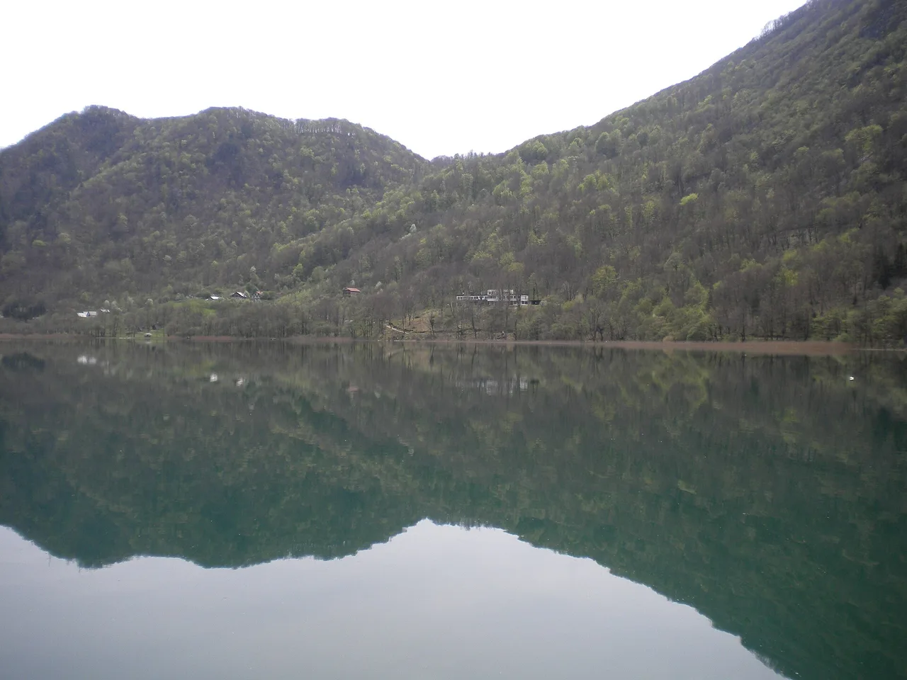The still surface of Boračko Lake reflecting forested mountains under a clear sky near Konjic