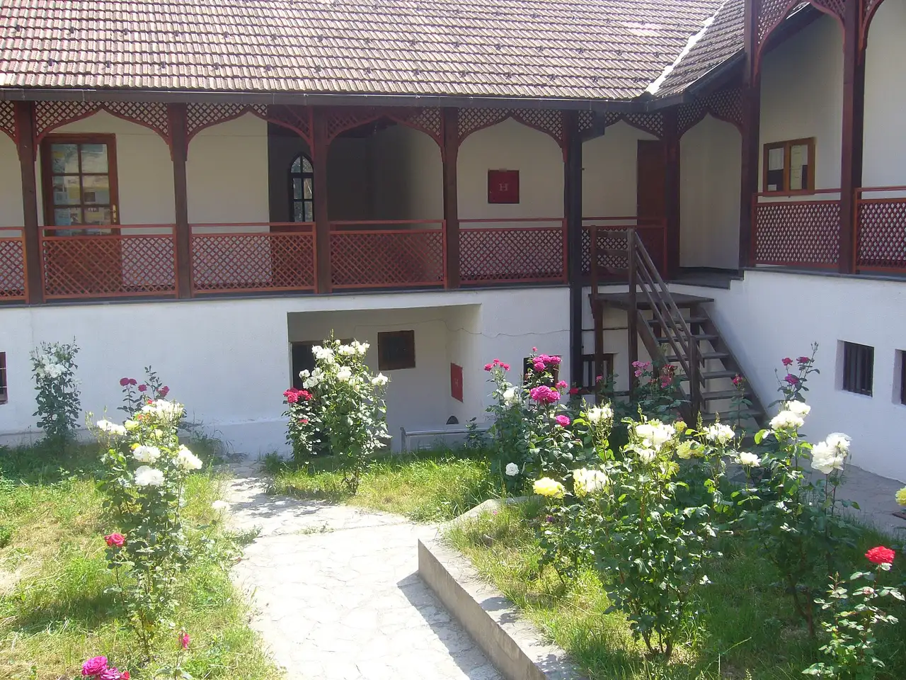 The garden courtyard of a restored Ottoman-era house in Konjic, white walls and dark carved-wood balconies around a rose garden