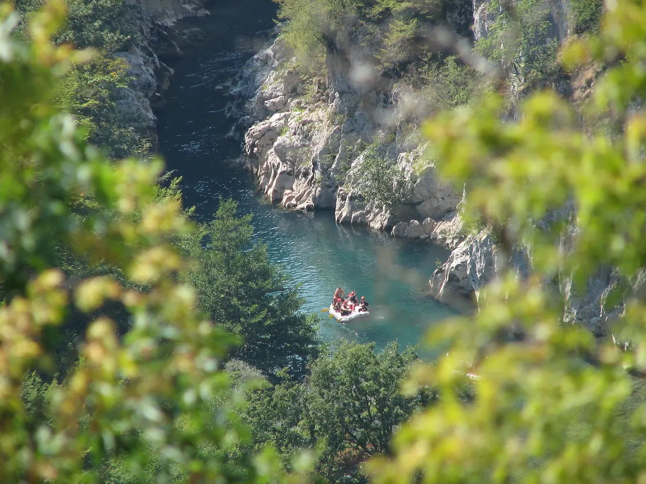 A raft of paddlers in helmets and life jackets running green whitewater on the Neretva between steep canyon walls