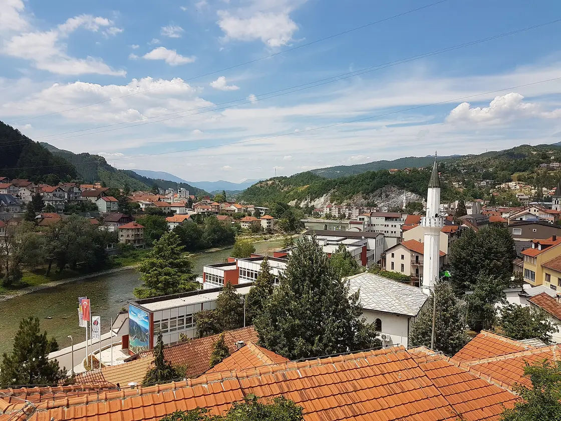 Red-tiled rooftops of Konjic with a minaret and the Neretva river beyond, green hills rising behind