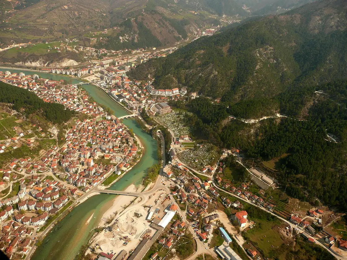 Aerial view of Konjic spread along both banks of the Neretva river in its valley, the old bridge and rooftops below wooded mountains