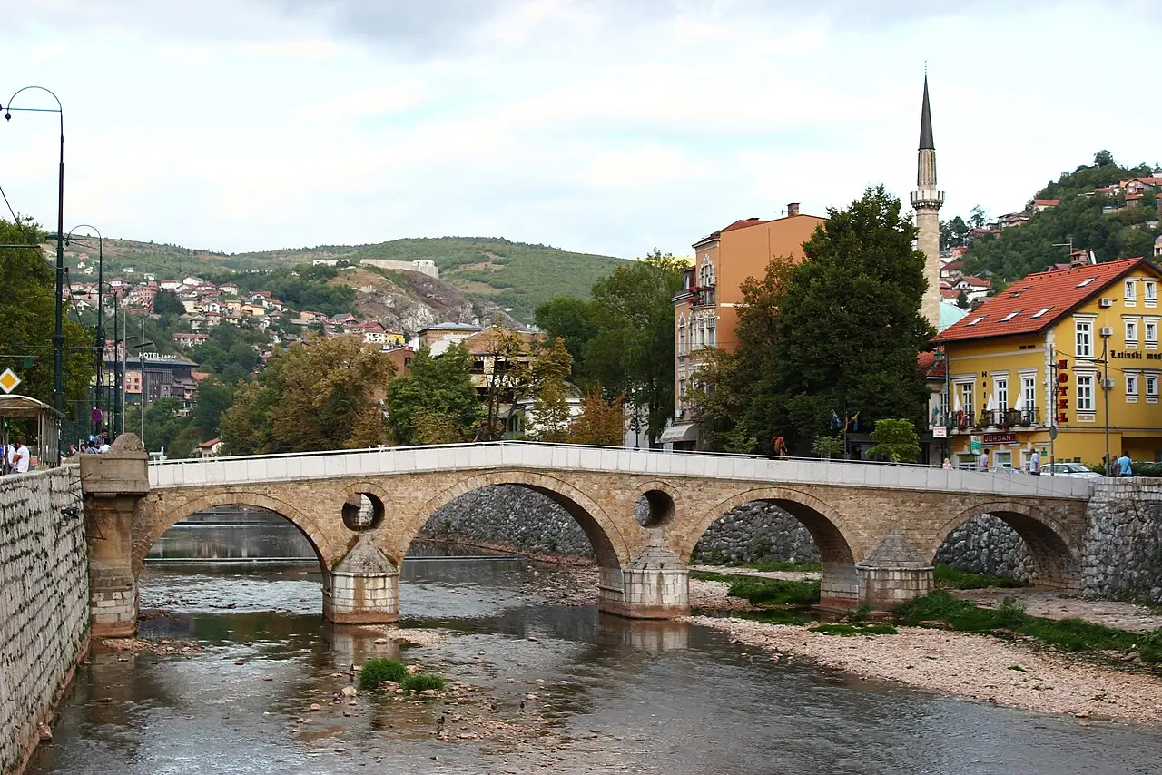 A wide view of the Latin Bridge over the Miljacka with a minaret and wooded hillside behind