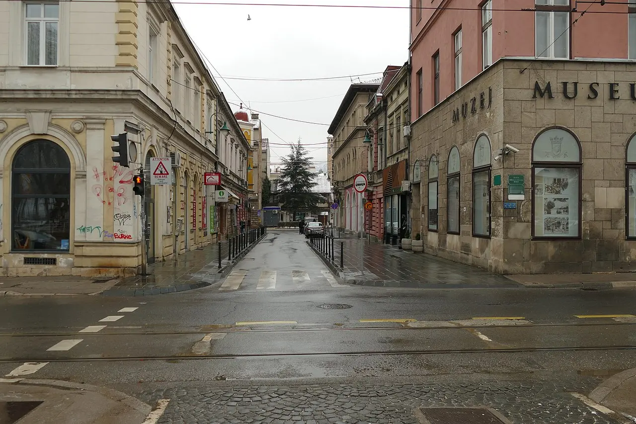 A rainy street corner in Sarajevo with the Museum of Sarajevo 1878-1918 sign on the building where Franz Ferdinand was shot in 1914