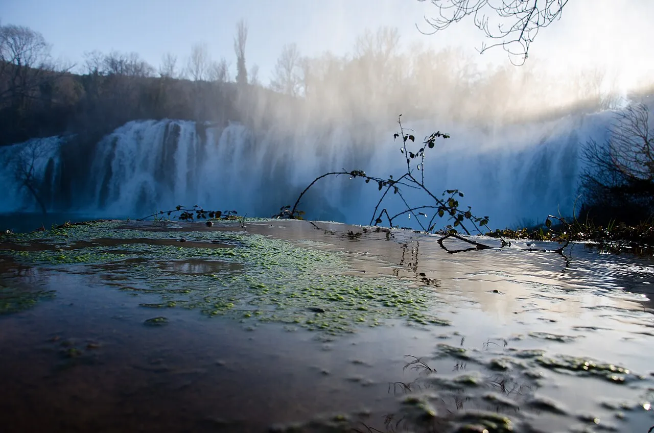The wide misty curtain of Kravice waterfalls dropping over a travertine ledge in Herzegovina, backlit by low sun