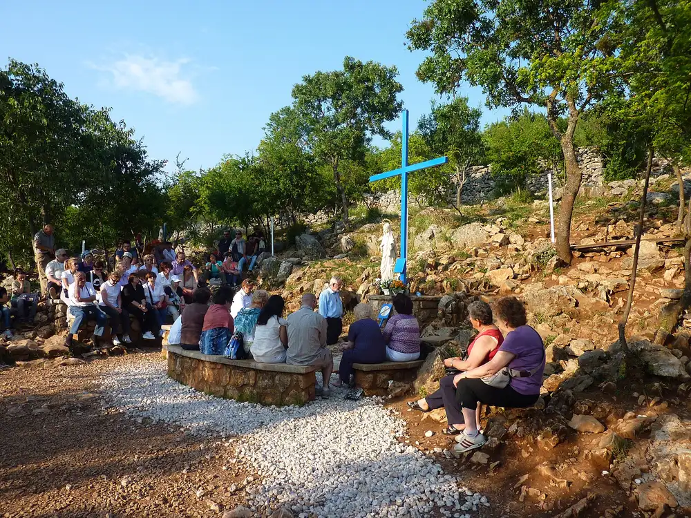 The Blue Cross prayer spot at the foot of Apparition Hill in Medjugorje, ringed by low stone walls and greenery