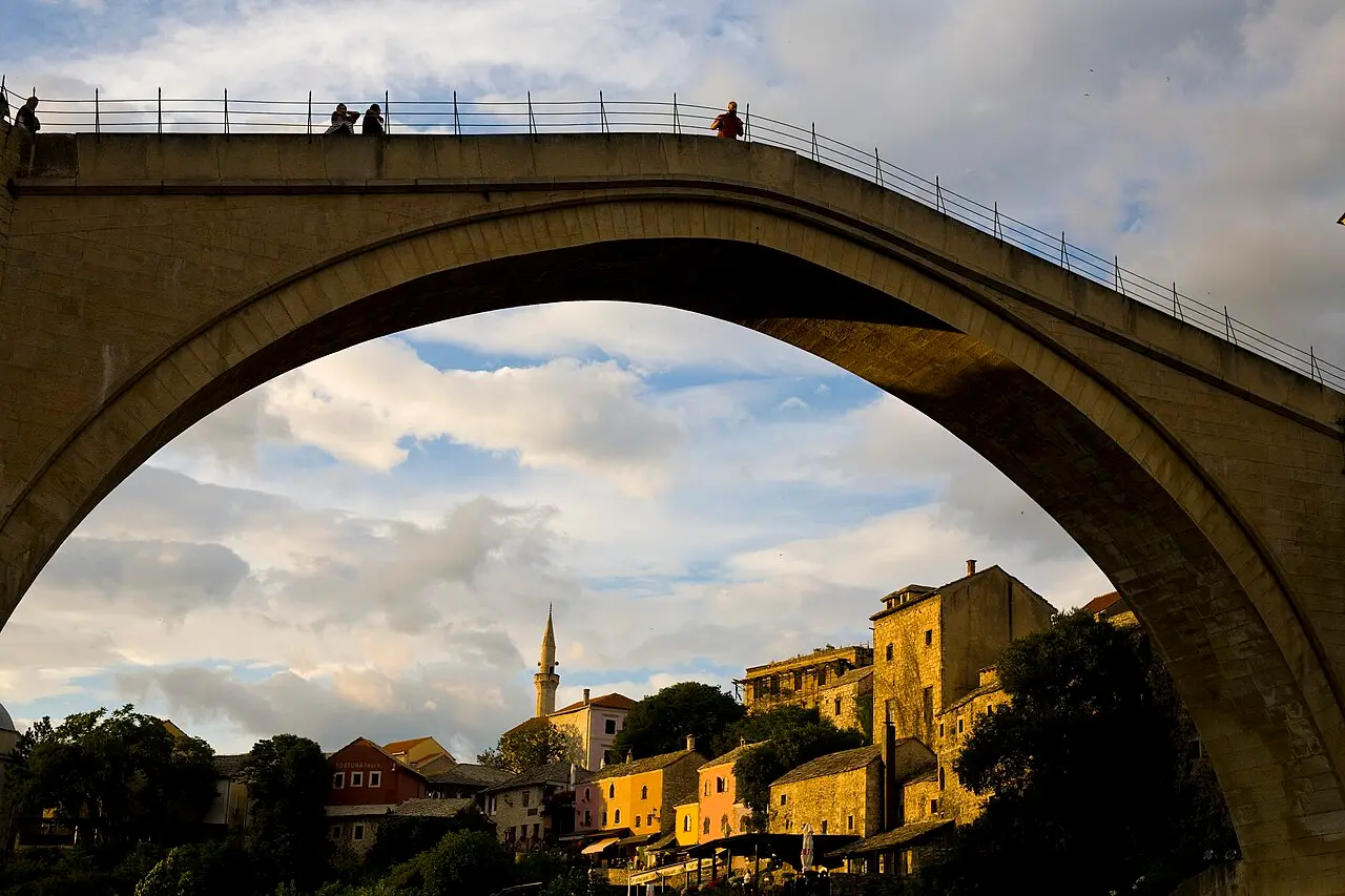 Stone arch of Mostar Old Bridge framing hillside houses and a minaret