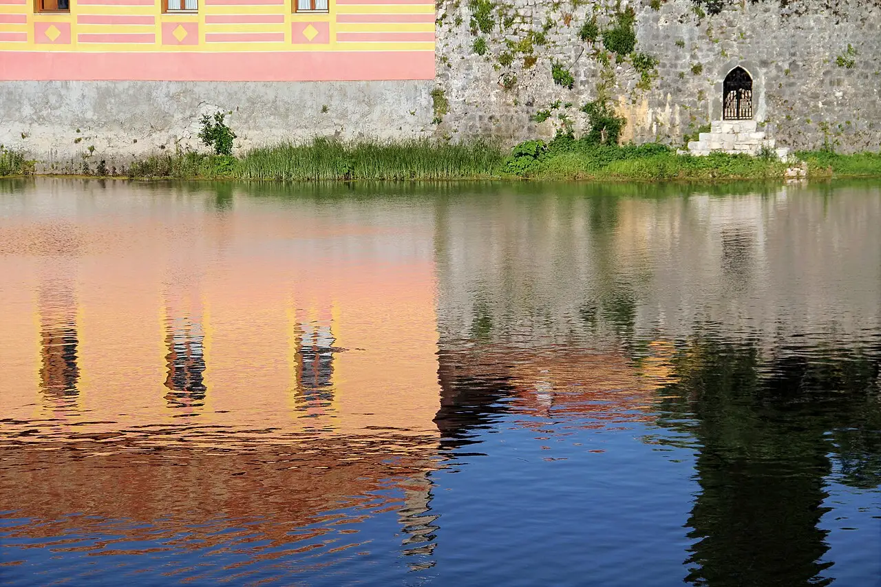 Old Town stone wall and a pink-and-yellow facade reflected in the Trebišnjica
