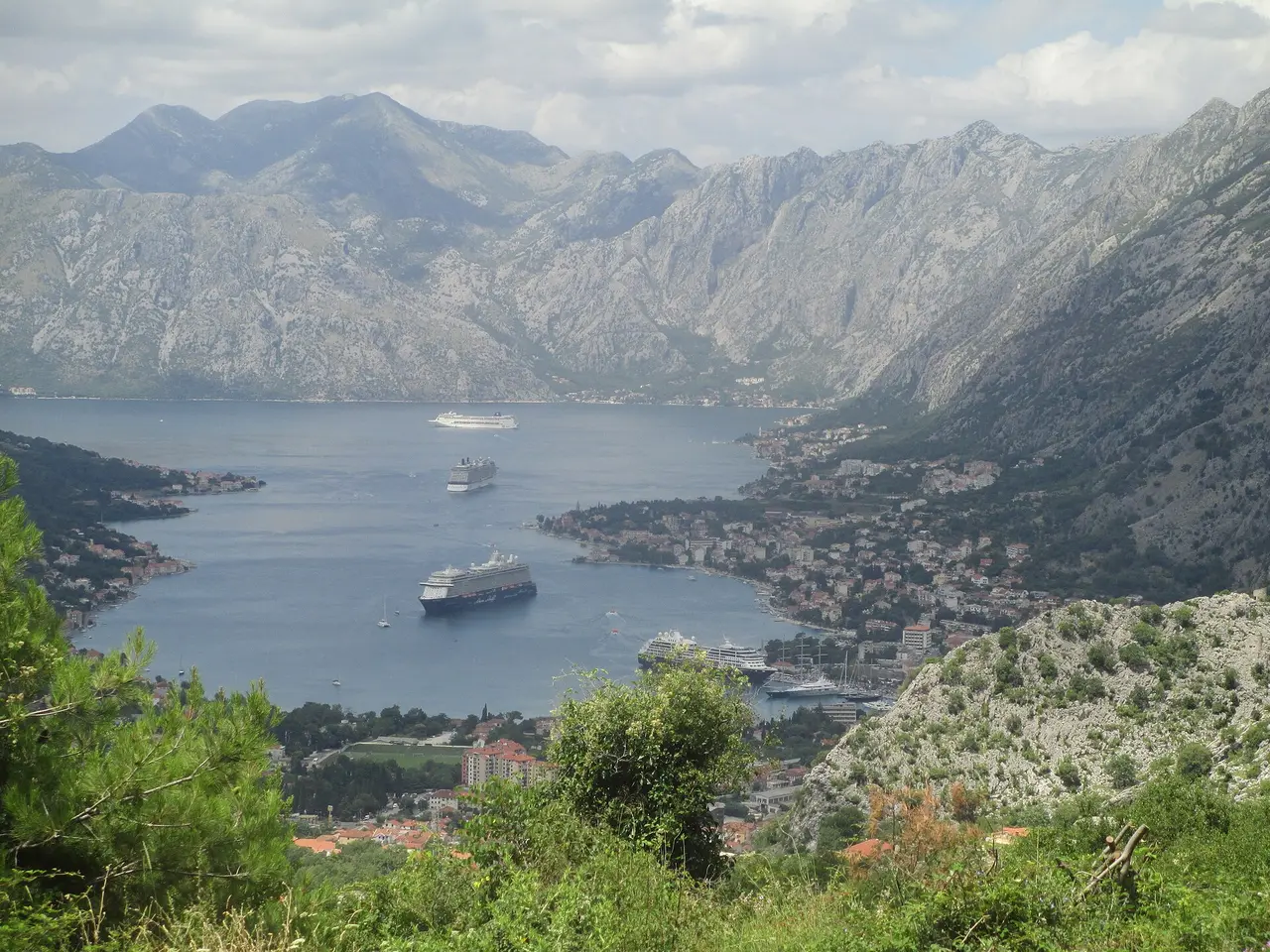 The Bay of Kotor seen from the mountain road above, cruise ships on the blue water and the town at the foot of steep grey peaks