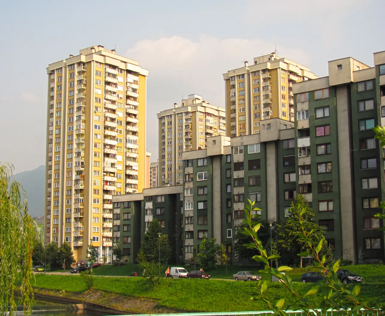 Yellow and green residential tower blocks in Sarajevo seen from the bank of the Miljacka river
