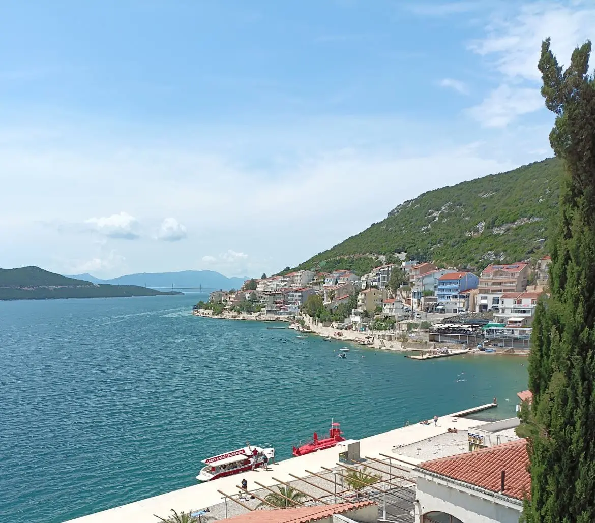 Turquoise Neum bay with the town along the far shore, a red excursion boat at a jetty and the Peljesac Bridge in the distance