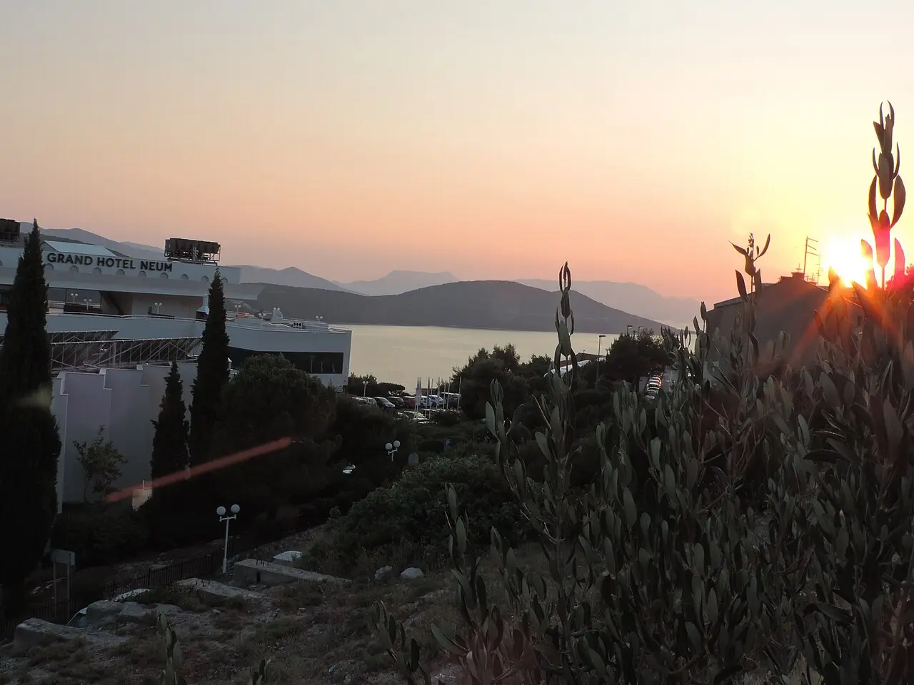 The Grand Hotel Neum on the hillside above the bay at sunset, with cypresses and olive trees in the foreground