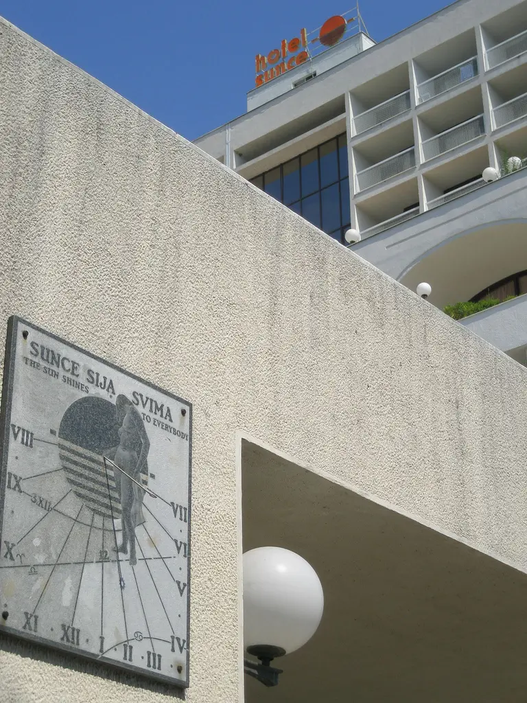 The Hotel Sunce sign above a modernist white hotel in Neum, with a stone sundial reading The Sun Shines to Everybody