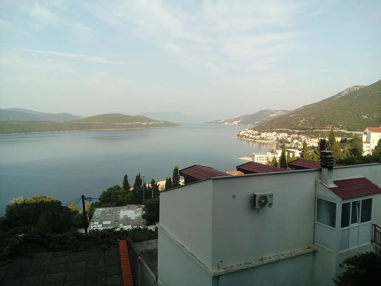 Elevated view over the long Neum bay with the town and its hotels curving along the far green shore under a soft sky