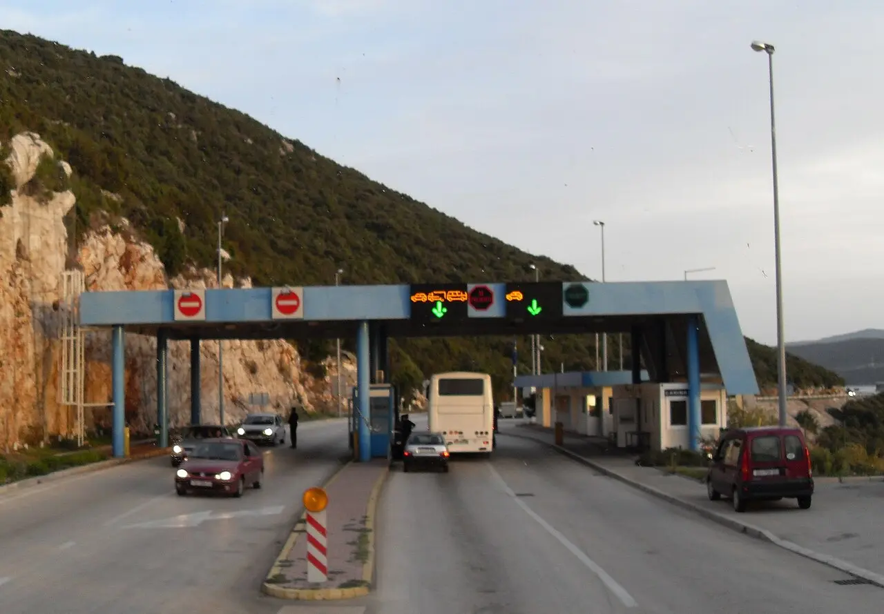 Cars and a coach at the Neum-Klek border checkpoint with lane signals under a hillside