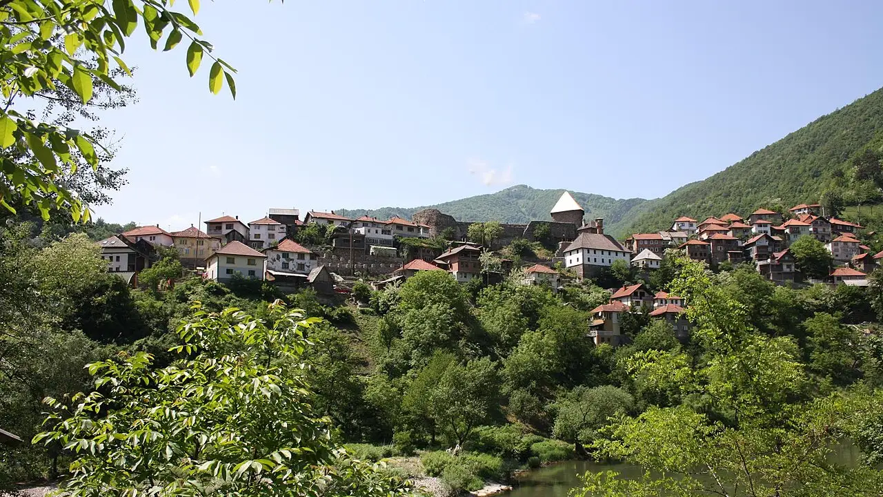 The village of Vranduk climbing a green hillside above the Bosna river, the conical white roof of the fortress keep crowning the ridge