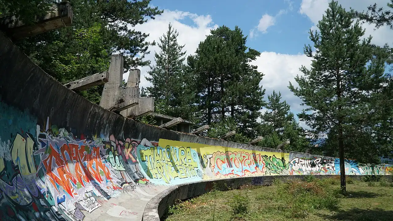 The banked concrete channel of the abandoned 1984 Olympic bobsled track on Trebević, covered in layered graffiti, forest on both sides