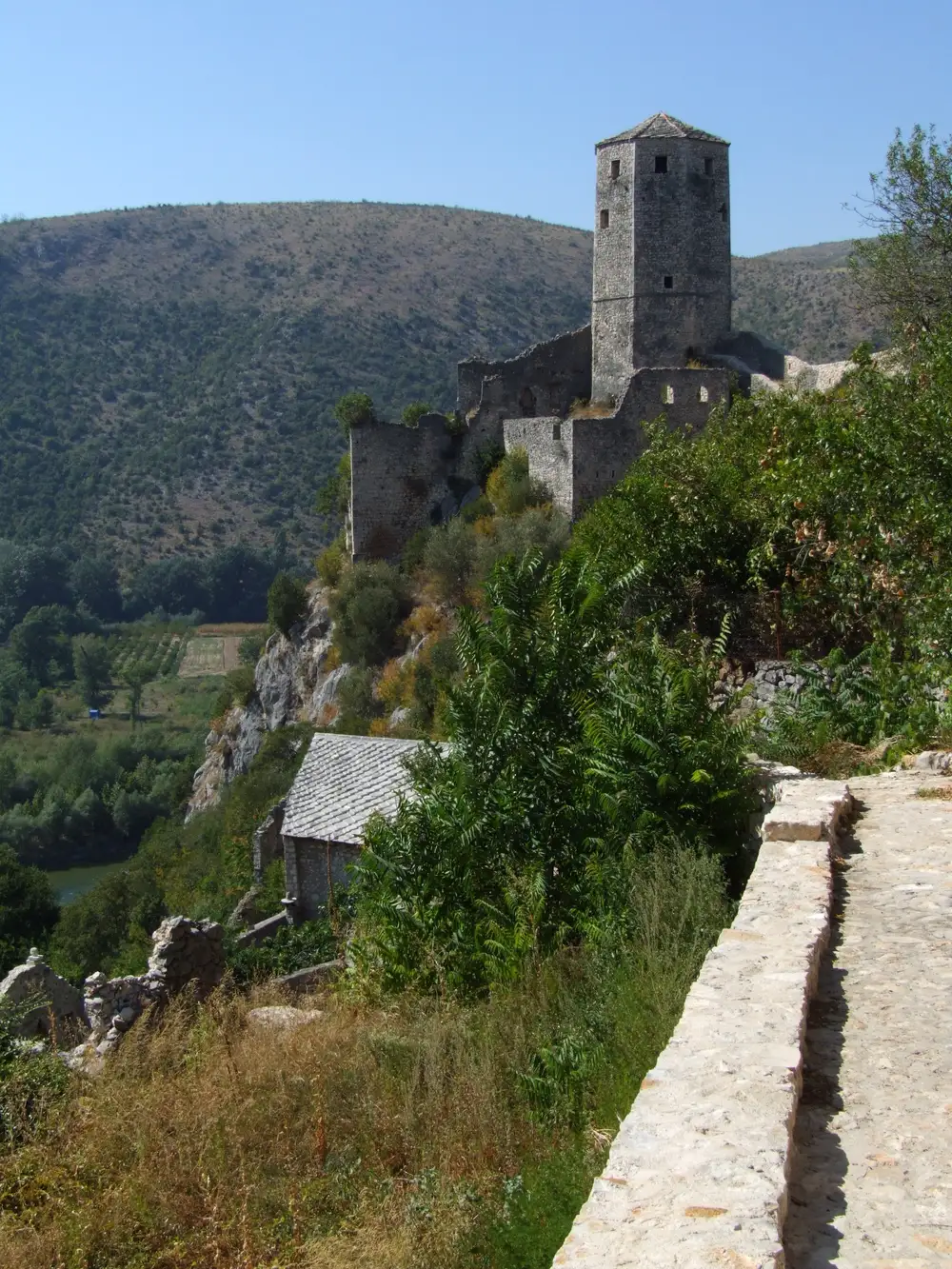 The cylindrical stone Kula tower and ruined fortress walls of the Počitelj citadel on the cliff top