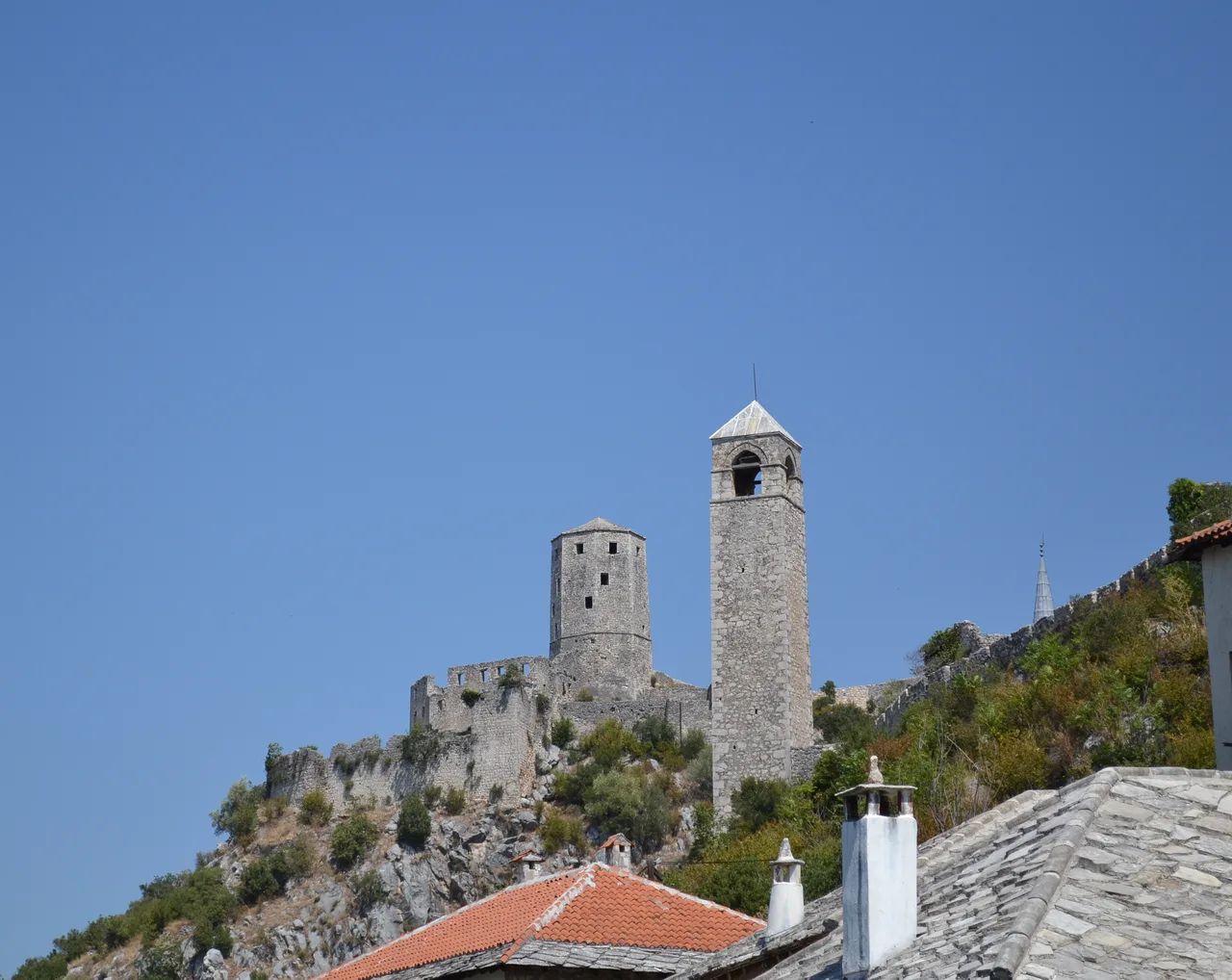 The silo-shaped Kula keep and the square Sahat-kula clock tower of Počitelj standing against a blue sky above the town walls