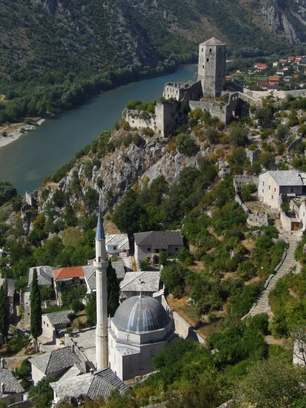 A general view over the pale stone rooftops and terraced walls of Počitelj climbing the hillside