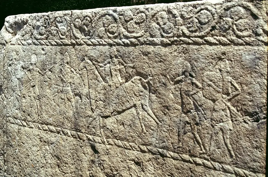 Shallow engraved scene on a stecak at Radimlja with a mounted rider carrying a lance, standing figures and a twisted rope border
