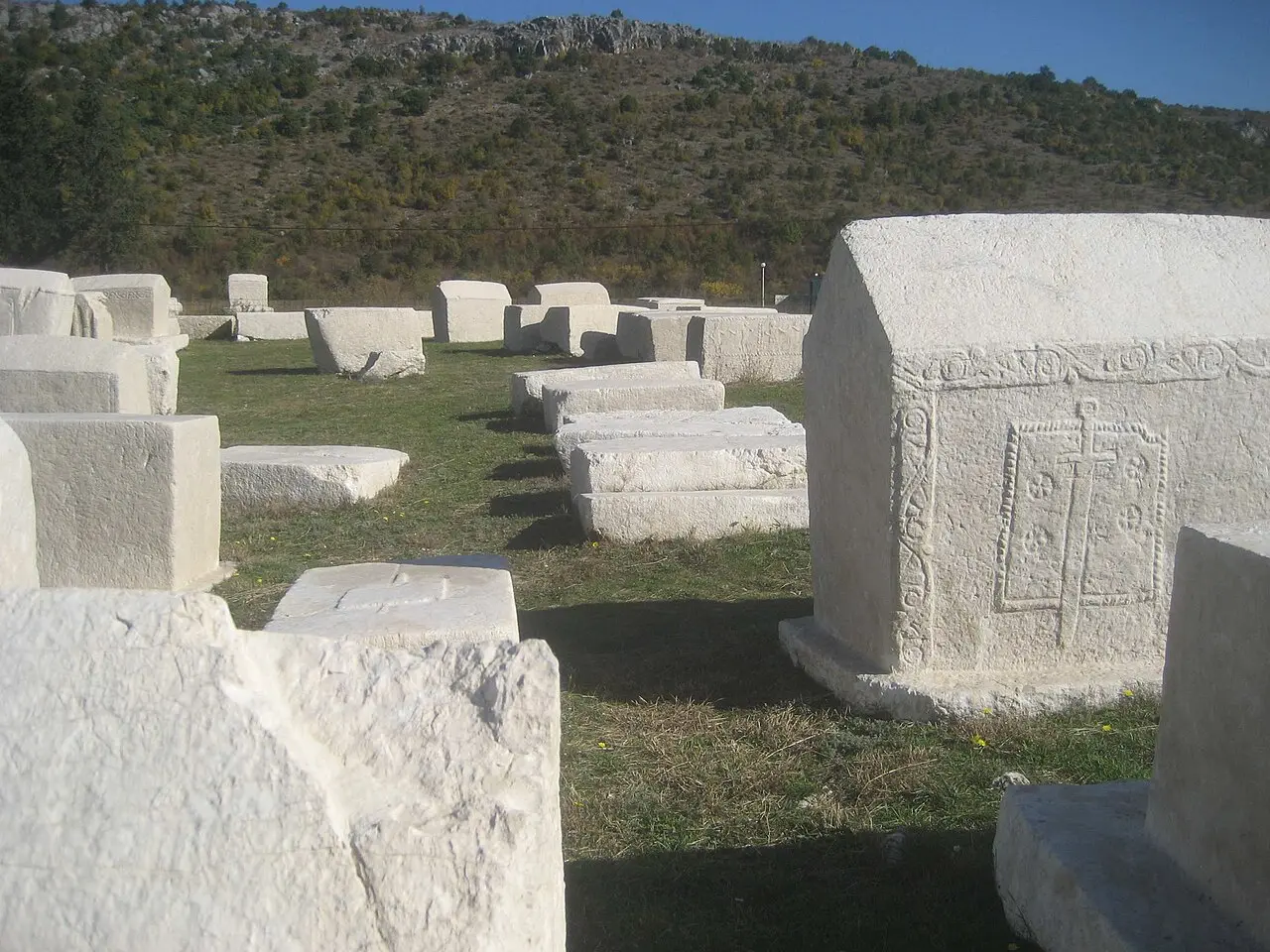 Stecci at Radimlja in autumn light with a bare karst hillside rising directly behind the necropolis