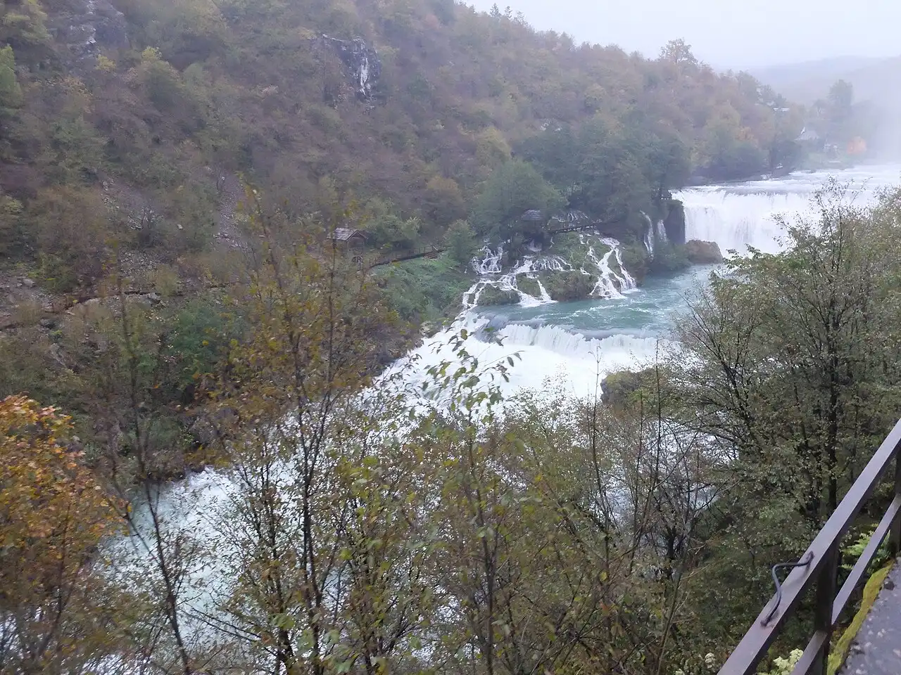The emerald-green Una river running over low tufa cascades through forest near Bihać, clear pools below