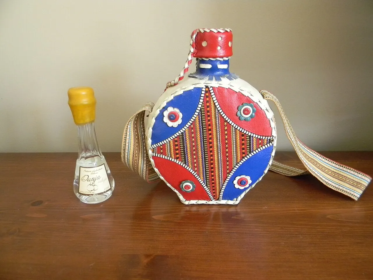A traditional embroidered leather rakija flask next to a small bottle of quince, dunja, rakija