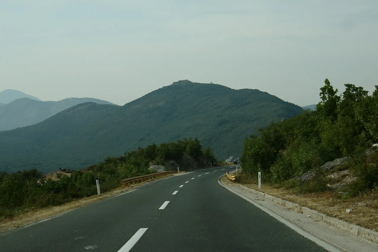 An empty two-lane road curving through green karst hills in Herzegovina on the way to Trebinje, the kind of drive a Croatian hire car reaches once the paperwork is sorted