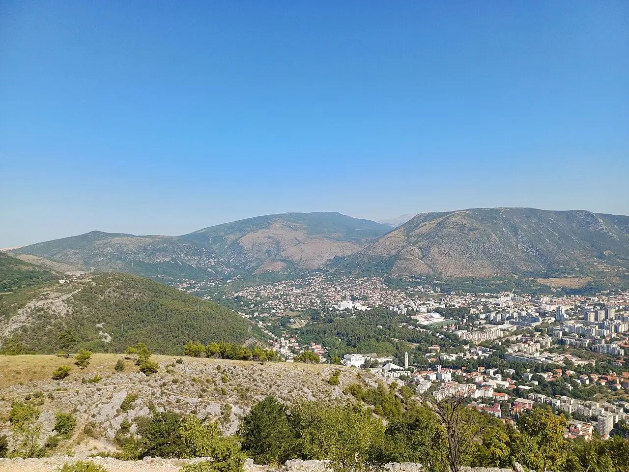A panorama of Mostar with minarets and red roofs under bare limestone mountains, a common destination for a Croatian hire car crossing into Bosnia