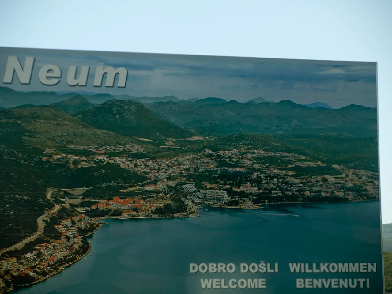 A welcome sign for Neum showing the town spread along its bay, the short strip of Bosnian coast that the old road passes through