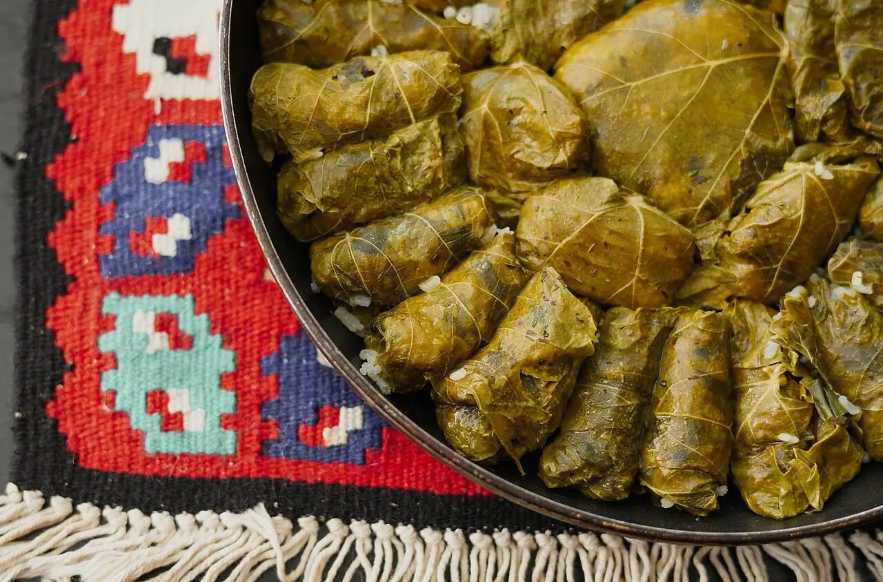 A round pan of japrak, vine leaves rolled around rice and minced meat, resting on a red and blue Bosnian kilim rug
