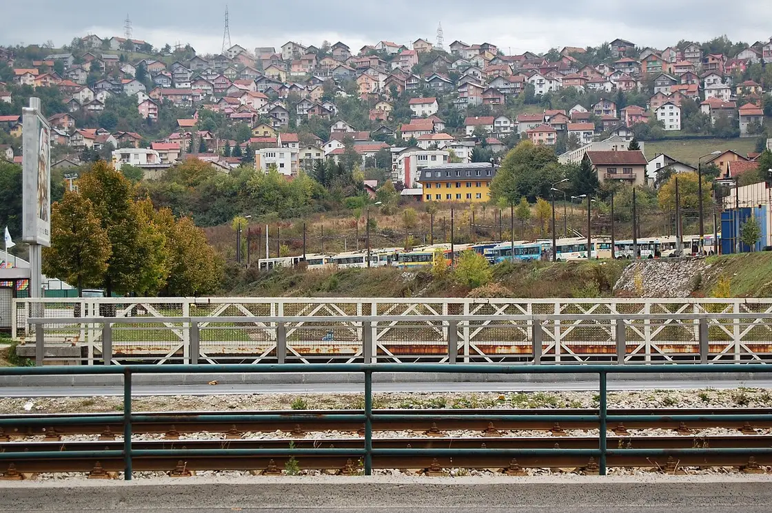 Sarajevo trams parked beside the tracks with the residential hills rising behind, part of the city transport network once you reach the centre