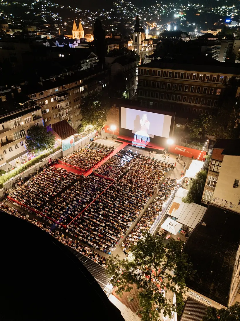 Aerial night view of the Open Air Cinema crowd and red carpet at the Sarajevo Film Festival, city lights and church spires behind