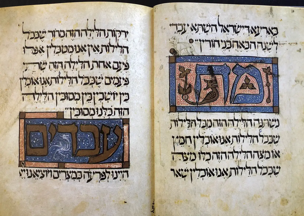 An open illuminated spread of the medieval Sarajevo Haggadah, with Hebrew script and decorated initial panels