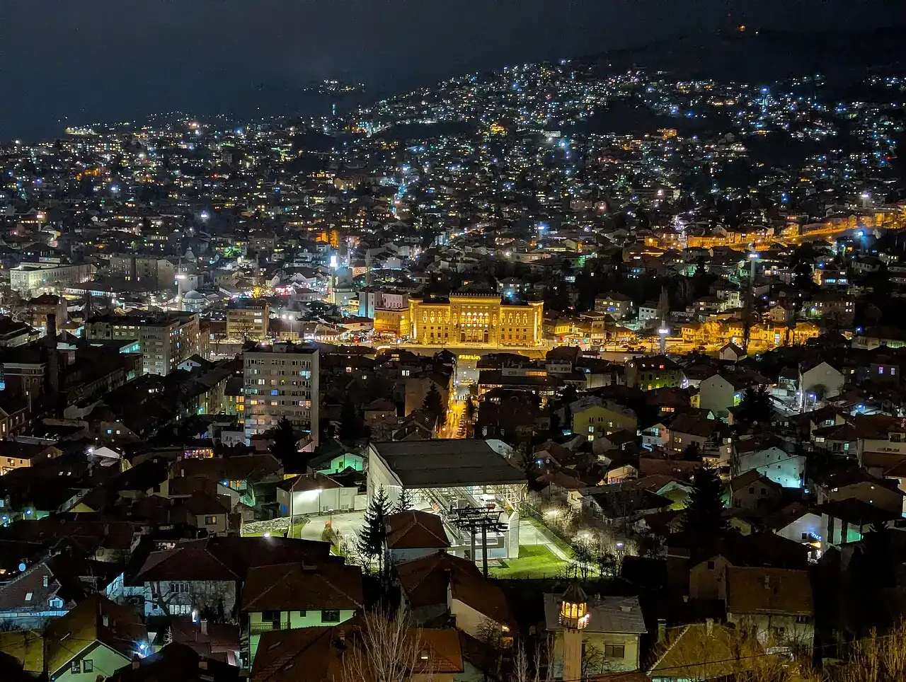 Wide night view of Sarajevo from a hillside with streets glowing in the valley