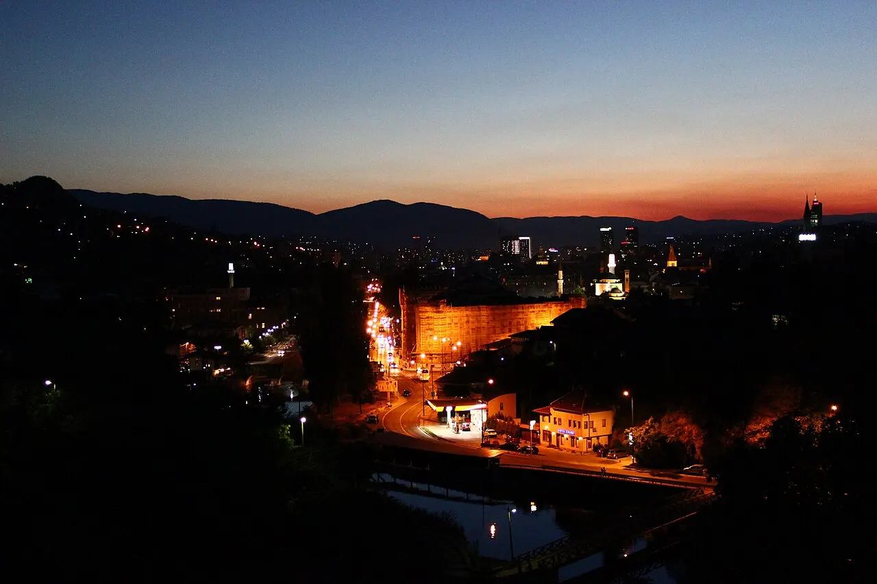 Sarajevo City Hall Vijećnica lit orange beside the Miljacka river at night